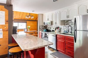 A modern kitchen with a marble countertop, stainless steel appliances, and red cabinetry.