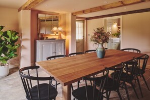 A dining area with a wooden table and black chairs, a potted plant, and a cabinet with a mirror. - Haymill Retreat - Luxury Cottages (Caersws)
