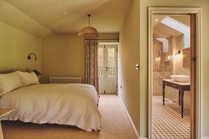 A bedroom with a large bed, a radiator, a hanging light fixture, and a view into a bathroom with a sink and mirror. - Haymill Retreat - Luxury Cottages (Caersws)