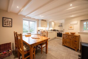 A kitchen with wooden cabinets, a dining table with chairs, and a large window. - Grimsbury Castle - Luxury Cottages (Hermitage)