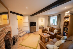 A living room with a fireplace, sofa, television, and a bookshelf. - Grimsbury Castle - Luxury Cottages (Hermitage)