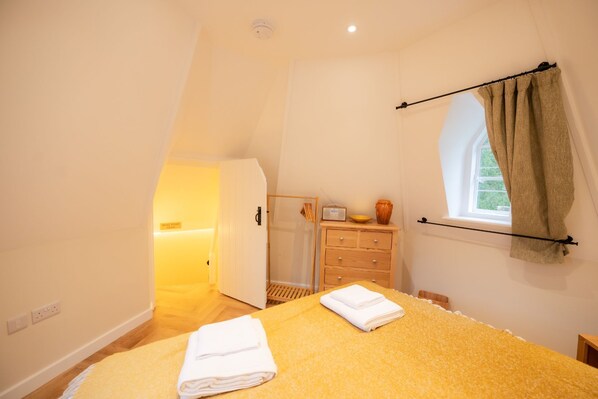 A bedroom with a bed, a dresser, a radio, and a window with curtains.