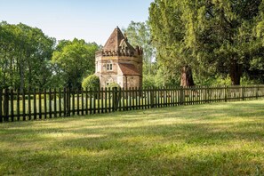 A historic stone tower with a conical roof, surrounded by a wooden fence and lush greenery.