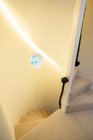 A staircase with beige carpeted steps, a white wall, and a black handrail. - Grimsbury Castle - Luxury Cottages (Hermitage)