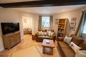 A cozy living room with a TV, sofa, coffee table, and bookshelf. - Grimsbury Castle - Luxury Cottages (Hermitage)