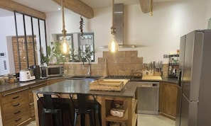 A modern kitchen with a central island, stainless steel appliances, wooden cabinetry, and hanging pendant lights. - Stone farmhouse in the heart of the Luberon (Ménerbes)