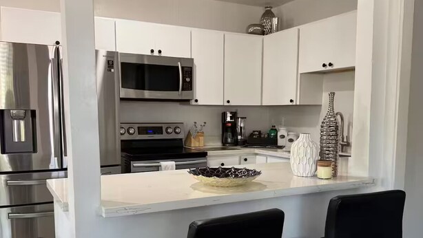 A modern kitchen with stainless steel appliances, a marble countertop, and two black bar stools. - Modern Lux Stay: Near Downtown, Sky Harbor and ASU (Phoenix)