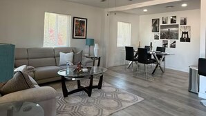 A spacious living area with a sofa, coffee table, dining table, and chairs. There is a ceiling fan, a window with blinds, and a wall with framed pictures. - Modern Lux Stay: Near Downtown, Sky Harbor and ASU (Phoenix)