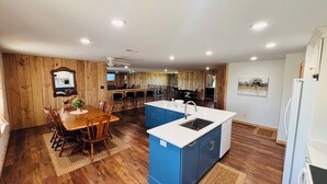 Une cuisine moderne avec un plancher en bois, un coin repas avec une table et des chaises en bois, un îlot central bleu doté d’un évier et d’un réfrigérateur.