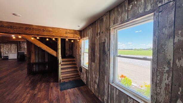 Un intérieur rustique avec un escalier en bois, de grandes fenêtres et une vue sur l’extérieur.