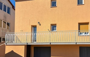 Ein Gebäude mit gelber Fassade, einem Balkon mit Metallgeländer und mehreren Fenstern.