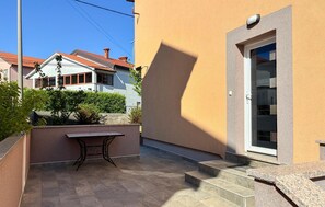 Ein Wohngebäude mit einer gefliesten Terrasse, einem kleinen Tisch und einer Tür, die in einen Innenbereich führt.