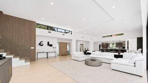 Uma sala de estar ampla com um conjunto de sofá branco moderno, uma área de jantar e uma cozinha visível através de um espaço aberto.