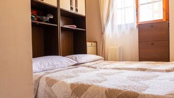 A bedroom with two beds, a wardrobe, and a window with curtains.