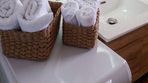 Un baño con un lavamanos blanco, dos cestas de mimbre con toallas blancas, un dispensador de jabón verde y un espejo redondo.