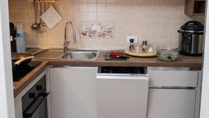 Una cocina compacta con armarios blancos, un lavamanos de acero inoxidable, una estufa y un lavavajillas.