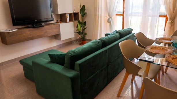 Una sala de estar moderna con un sofá verde, un televisor de pantalla plana, una mesa de comedor con sillas y una planta en maceta.