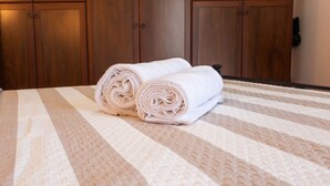 Una cama con toallas enrolladas y un armario de madera al fondo.