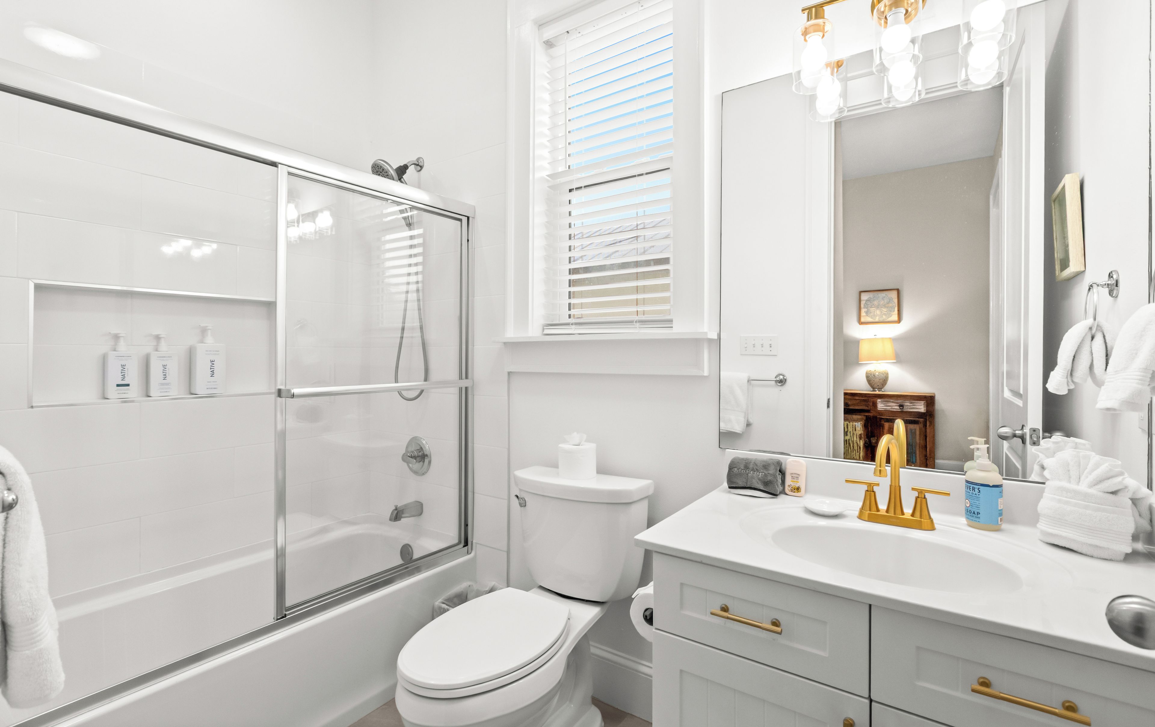 Un baño moderno con ducha envuelta en vidrio, inodoro y tocador con lavamanos y espejo.