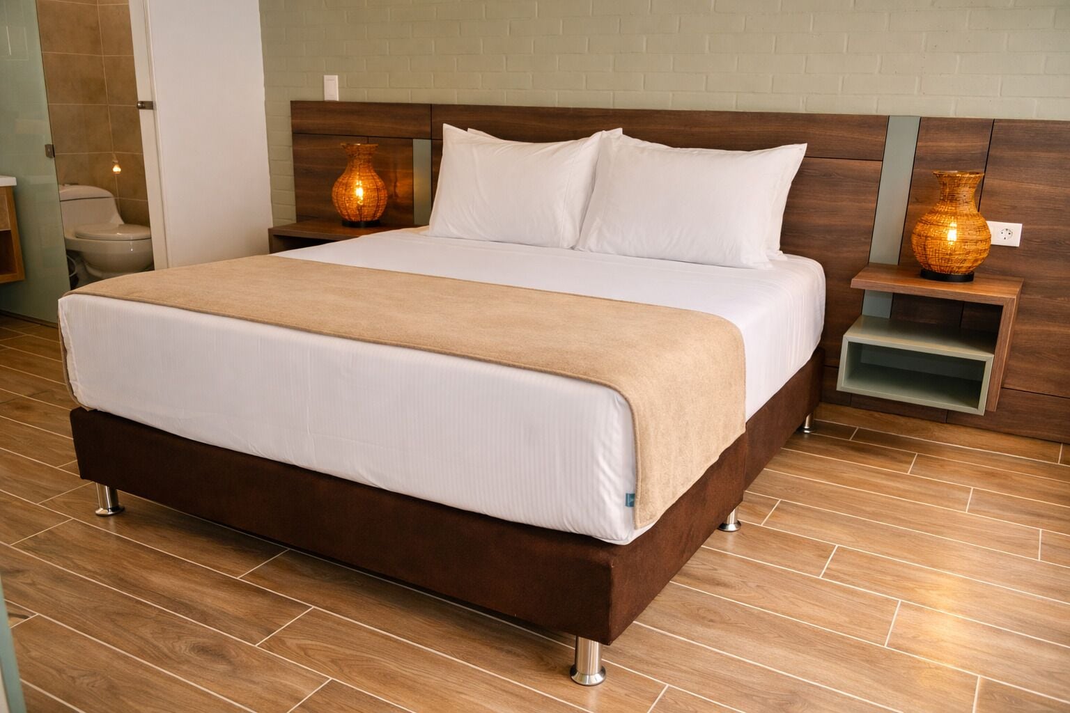Une chambre d’hôtel avec un grand lit, une tête de lit en bois, des tables de chevet et un sol carrelé.