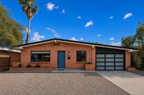 Ein eingeschossiges Backsteinhhaus mit Garage, einer blauen Tür und blauem Himmel.
