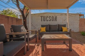An outdoor patio with a sofa, chairs, and a table, a brick wall with 'TUCSON' written on it, and a tree. - 2nd Street Tucson - Desert Modern Boutique Rental (Tucson)