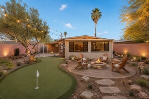 Ein modernes Haus mit Terrasse, Gartenmöbeln und einem Putting Green.