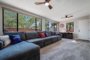 A modern living room with a sectional sofa, large windows, and a ceiling fan. - 2nd Street Tucson - Desert Modern Boutique Rental (Tucson)