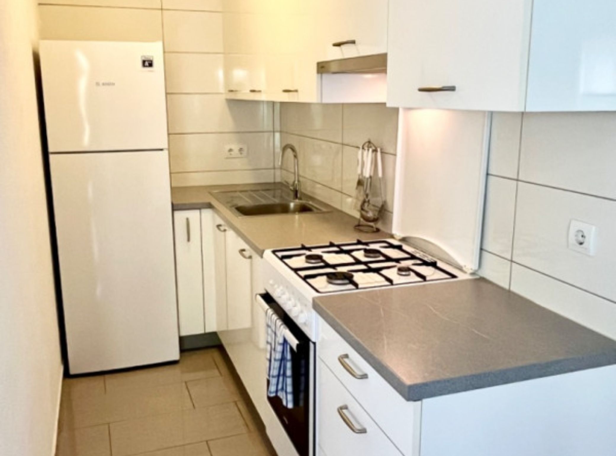 A compact kitchen with white cabinets, a stainless steel sink, and a gas stove.