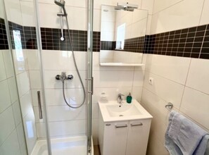 Ein Badezimmer mit Duschkabine aus Glas, einem weißen Waschbecken mit Spiegel darüber und einem Handtuch an der Wand.