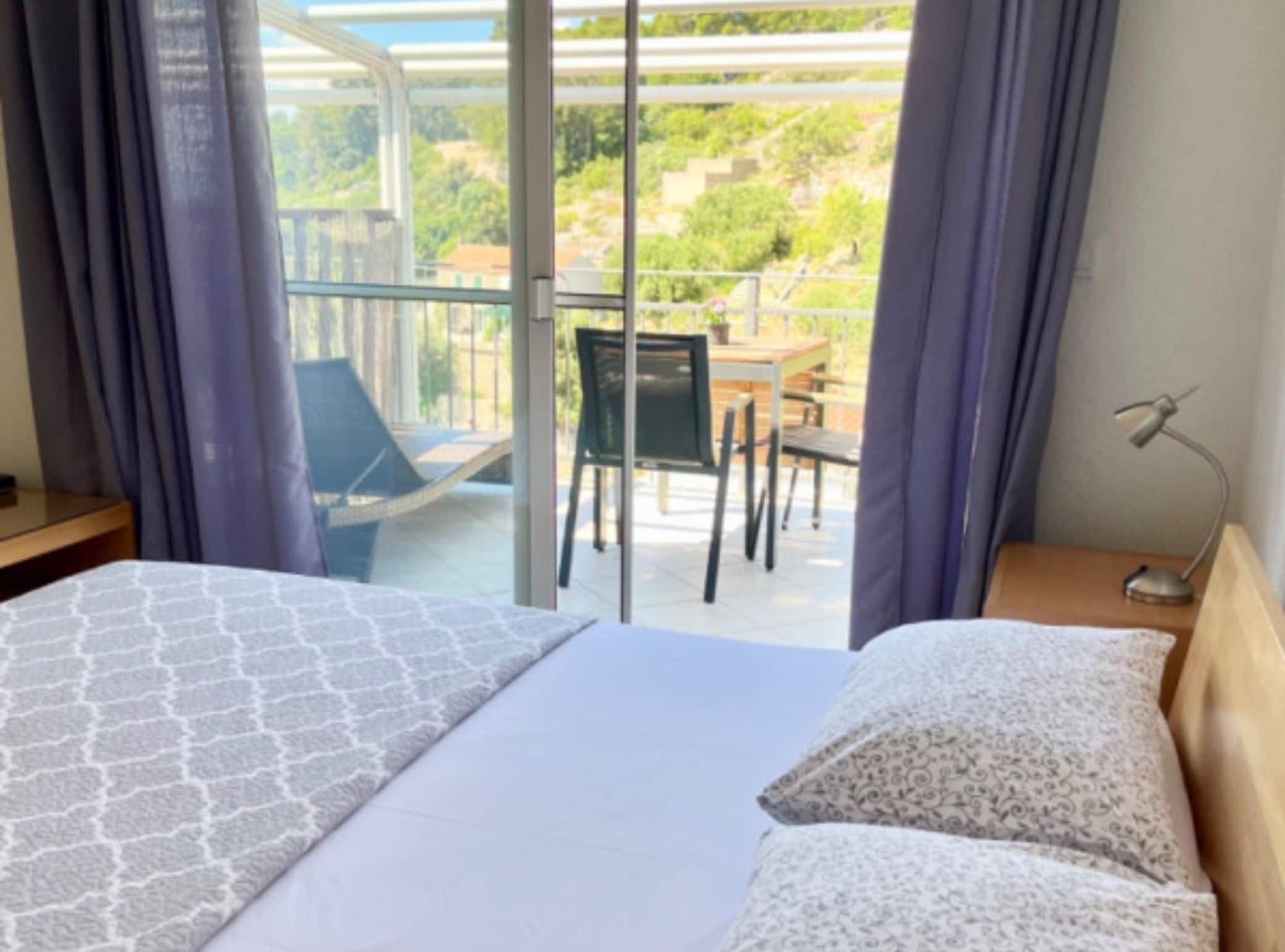 Ein Hotelzimmer mit Bett, Stuhl, Tisch und einem Balkon mit Blick auf Grünflächen.