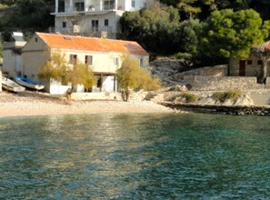 A coastal building with a tiled roof, situated by a body of water. - Paradise Apartments (Jelsa)