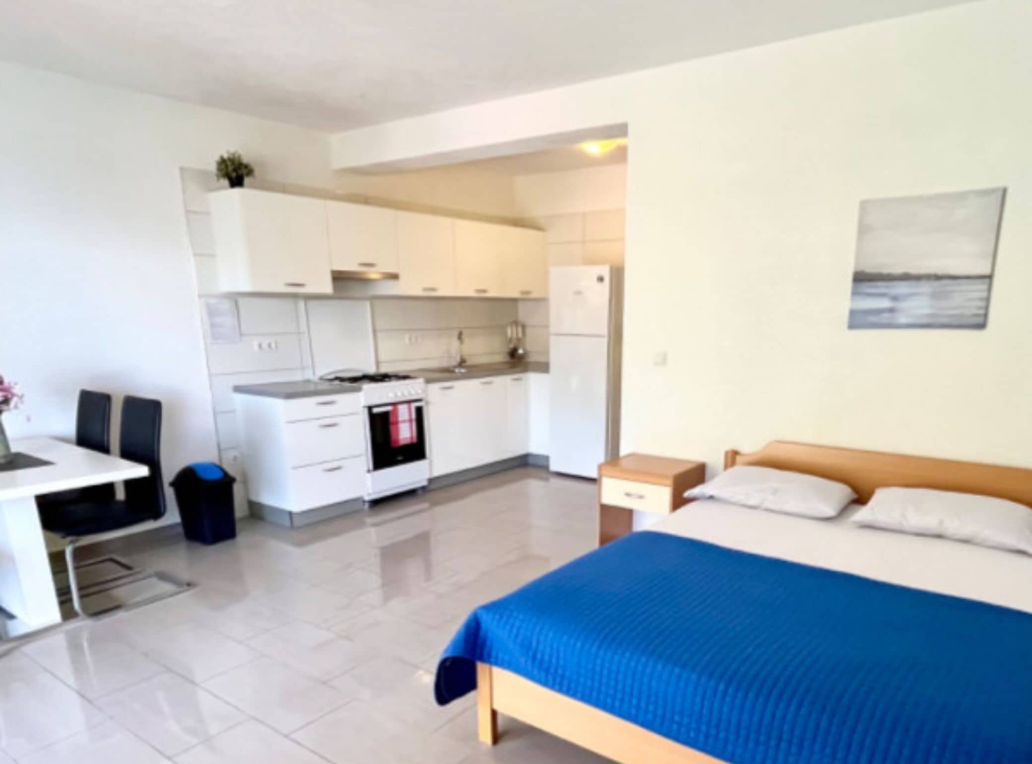 Ein kompaktes Hotelzimmer mit Bett, kleinem Schreibtisch, einer Küchenzeile und Meerblick.