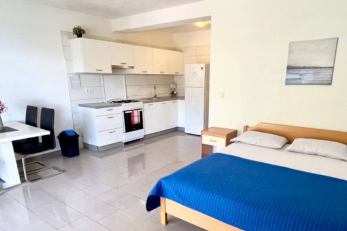 A compact hotel room with a bed, a small desk, a kitchenette, and a view of the sea.