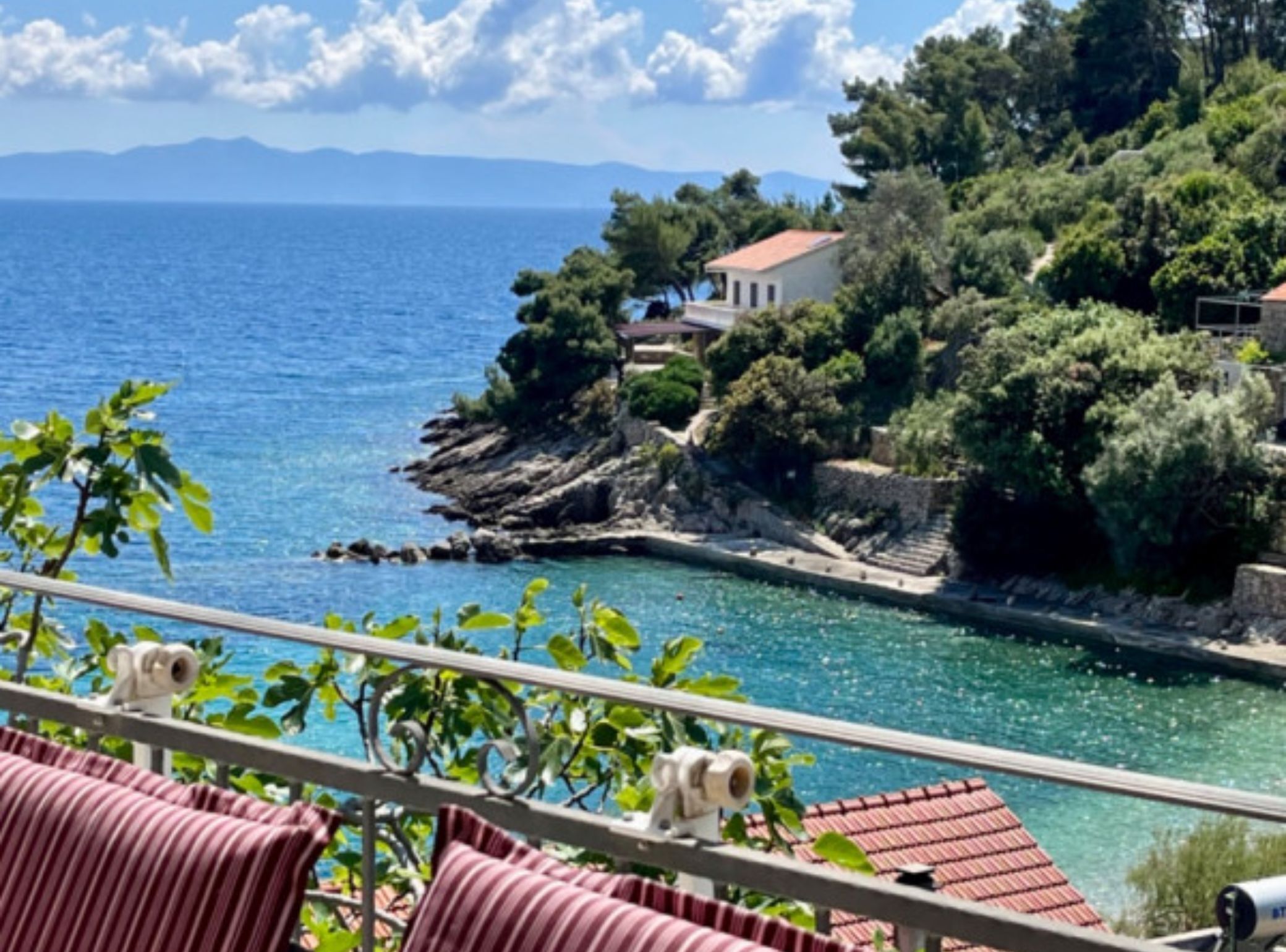 A coastal view with a balcony, a small building on a rocky outcrop, and a clear blue sea.