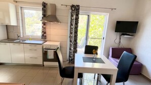 Cocina compacta con estufa, lavamanos y ventana. Hay una mesa de comedor con sillas y un televisor montado en la pared.