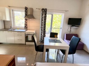 A compact kitchen with a stove, sink, and window. There is a dining table with chairs and a TV mounted on the wall. - Paradise Apartments (Jelsa)