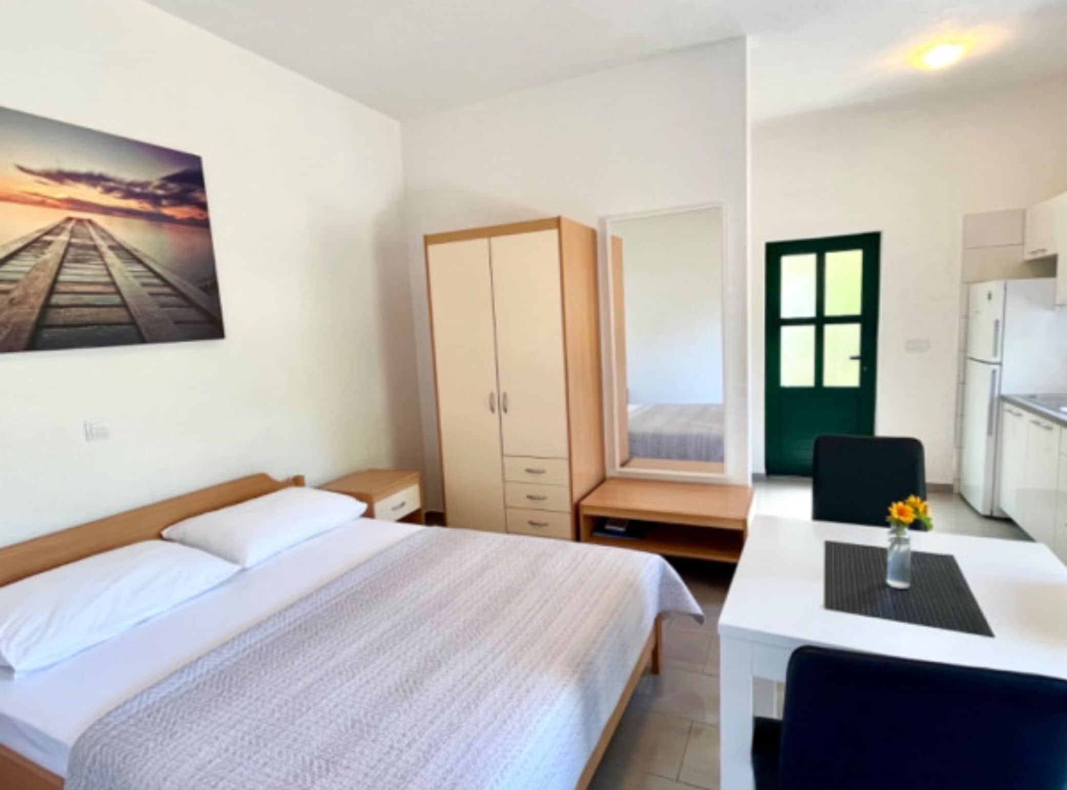 Ein Schlafzimmer mit Bett, Schrank, Schreibtisch mit Stuhl und Blick auf einen Sonnenuntergang durch ein Fenster.