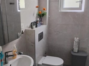 Ein Badezimmer mit Waschbecken, Toilette und einem kleinen Fenster mit Blumen.