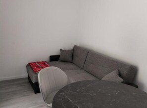 A grey sofa with a red plaid throw blanket, a round dark grey coffee table, and a white chair. - Comfort Apartments Orma (Povljana)