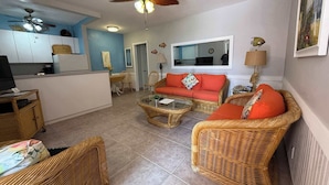 A living room with wicker furniture, a red sofa, a ceiling fan, and a kitchen area. - Oceanfront Escape on Hollywood Beach (Hollywood)