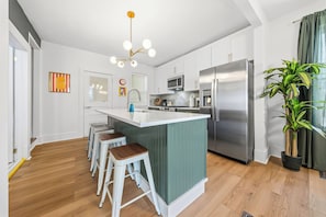 Una cocina moderna con una isla central, taburetes de bar, un refrigerador de acero inoxidable y una planta en maceta.