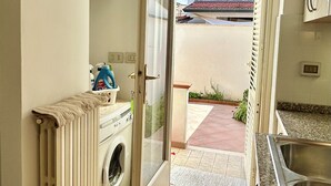 Une cuisine compacte équipée d’un lave-linge, d’un évier et offrant une vue sur la plage par une porte ouverte.