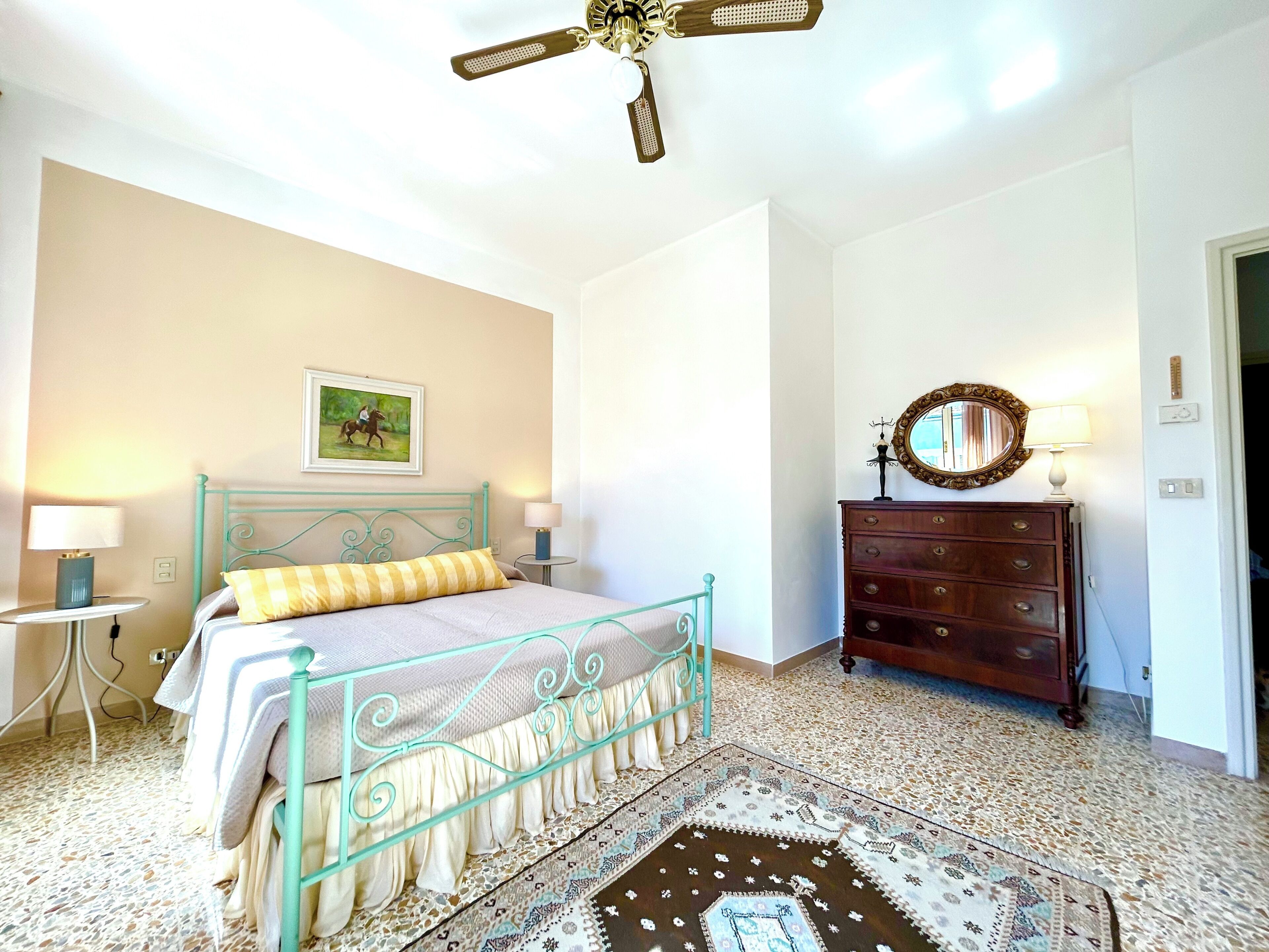 Un dormitorio con cama, cómoda, ventilador de techo, espejo montado en la pared y alfombra.