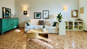 Un salon avec un canapé blanc, une table basse en bois, un meuble vert et des œuvres d’art accrochées au mur.