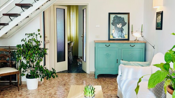 Un salon avec un escalier, un coin repas, un meuble turquoise et un canapé blanc.