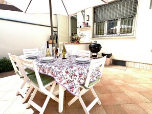A patio table set for dining with chairs, a grill, and a window with decorative items. - CasaMilla-Viareggio-villetta-mare-relax-6 places (Viareggio)