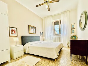 A bedroom with a bed, a nightstand, a dresser, a ceiling fan, a window with curtains, and a mirror. - CasaMilla-Viareggio-villetta-mare-relax-6 places (Viareggio)