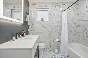 A modern bathroom with a white sink, mirror, toilet, and bathtub. - Three Waters Escape | 2 Kings | Game Lounge (Valparaiso)