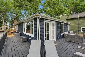 Une terrasse avec des meubles d’extérieur, un petit espace couvert et une maison aux bardages sombres et aux moulures blanches.